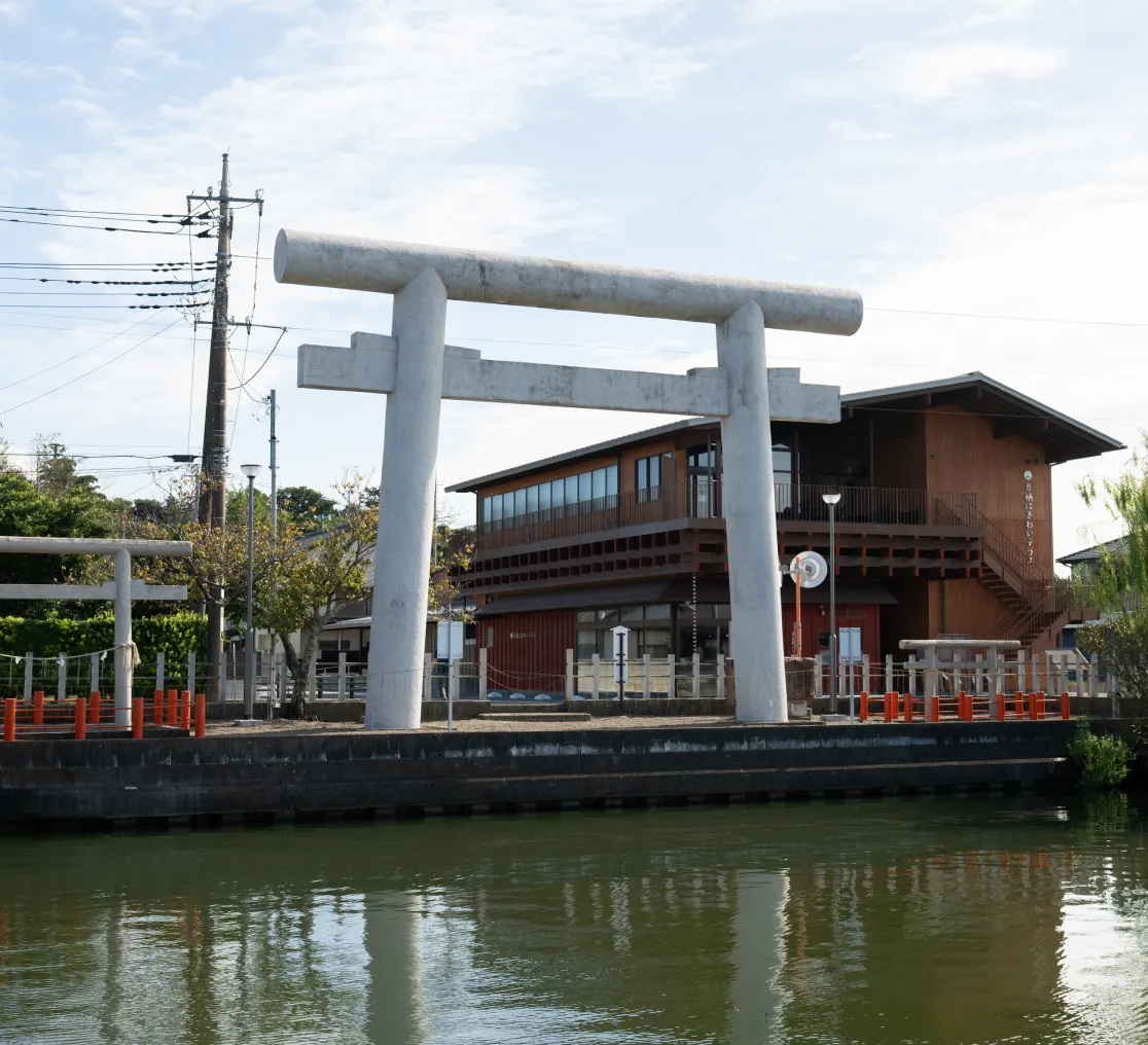 川沿いに大きな白い鳥居が建ち、静かな水面にその姿が映り込んでいる情景