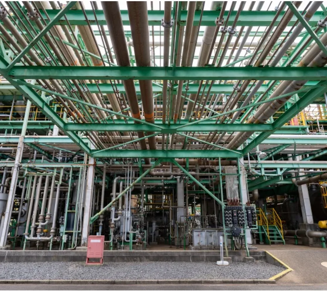 複数の金属製タワーが立ち並び、周囲に黄色や緑色の手すりが巡る工業プラントの設備