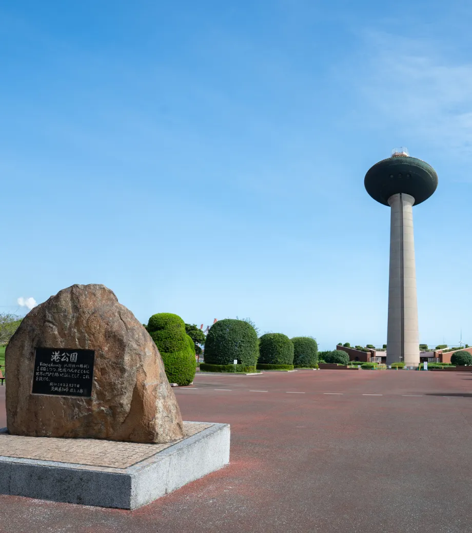 青空の下、広々とした公園に立つ大きな記念石と、その奥にそびえる塔のある開放的な景観